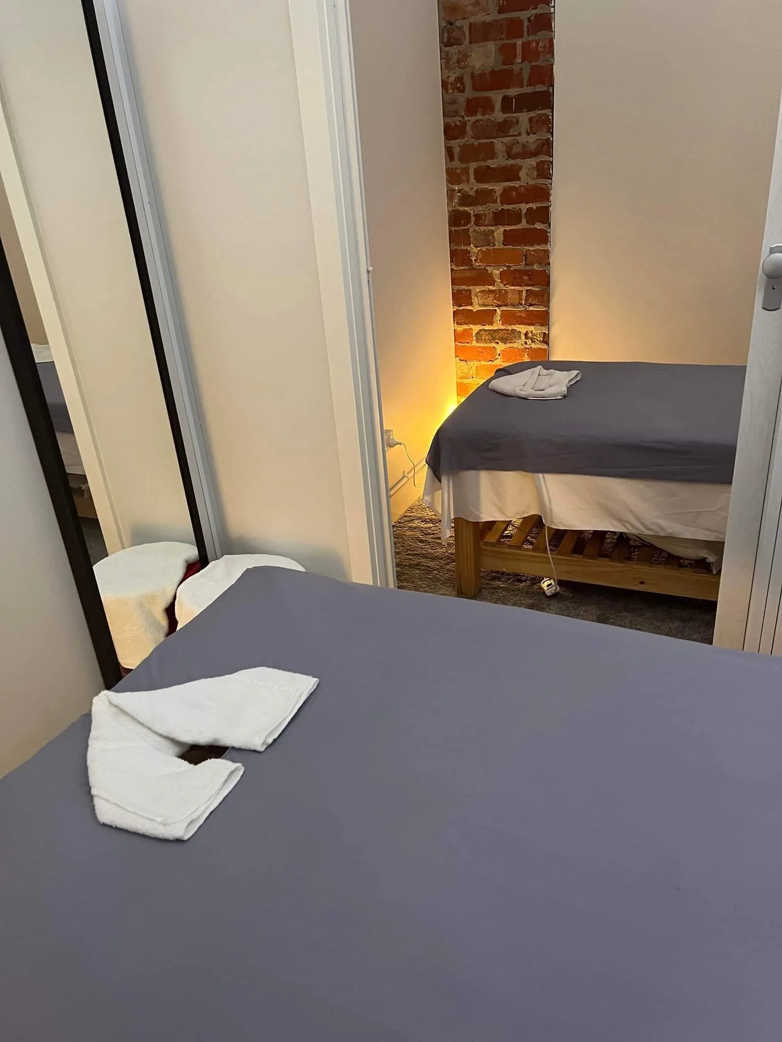 Two massage beds with folded white towels in warm lamplight, exposed brick column