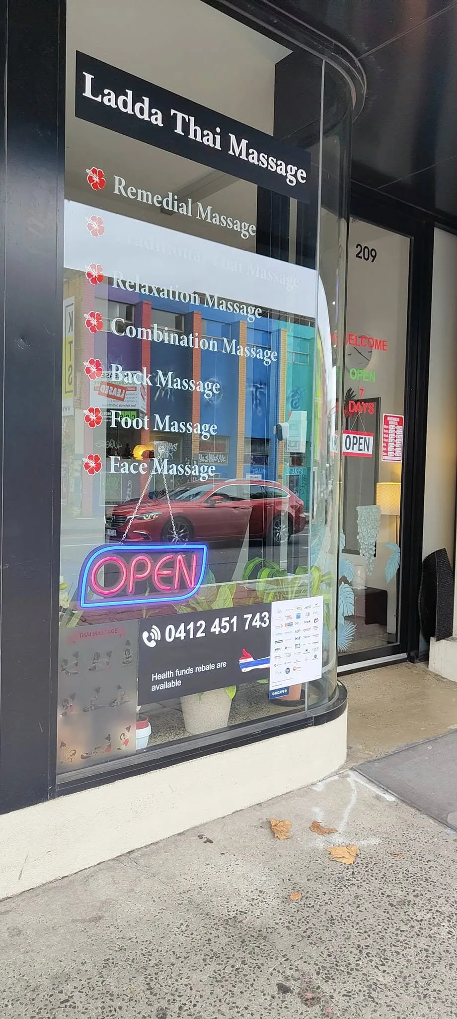 Ladda Thai Massage shopfront window at 209 Johnston St — service list, phone number and OPEN neon